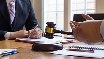 Attorney meeting with client at desk with gavel and legal documents.