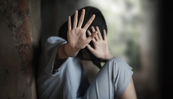 Frightened person raising hands defensively in a dark setting.
