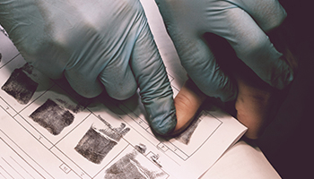 Gloved hands taking fingerprints on a police booking form.