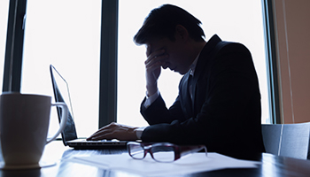 Stressed man working on laptop in a dim office.